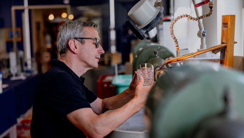 A man works on a glass at a grinding machine in a workshop.