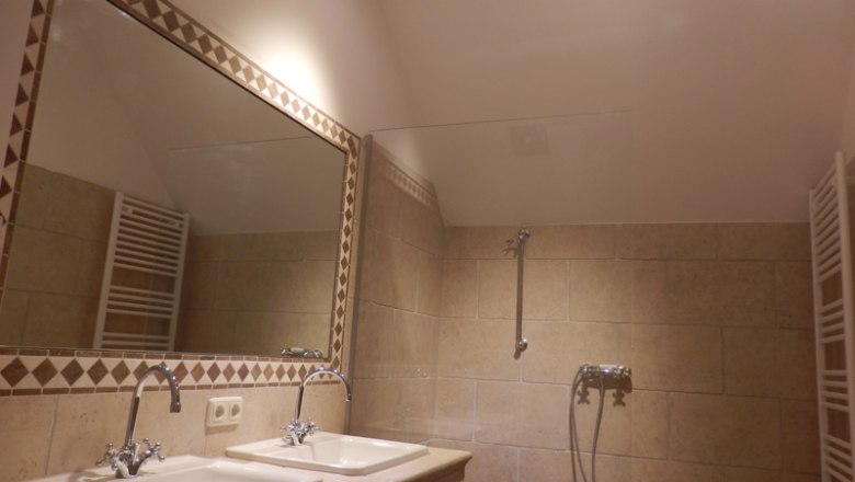 Bathroom with two washbasins, large mirror and beige tiled wall.
