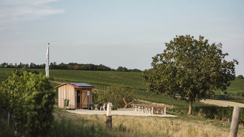 A small wooden hut with seating in a rural landscape.