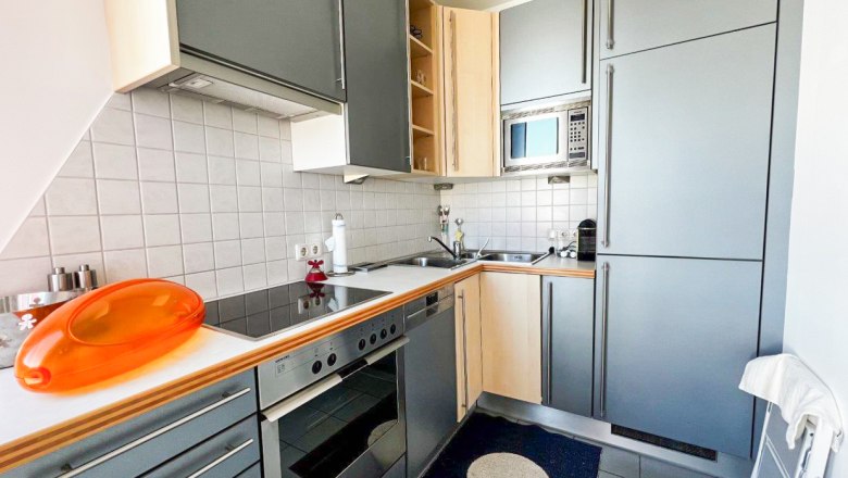 Modern kitchen with gray cabinets, stove, microwave and sink. An orange decorative item lies on the worktop.