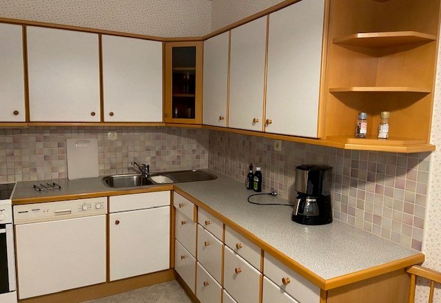 Kitchen with white cupboards, sink, coffee machine and tiled splashback.