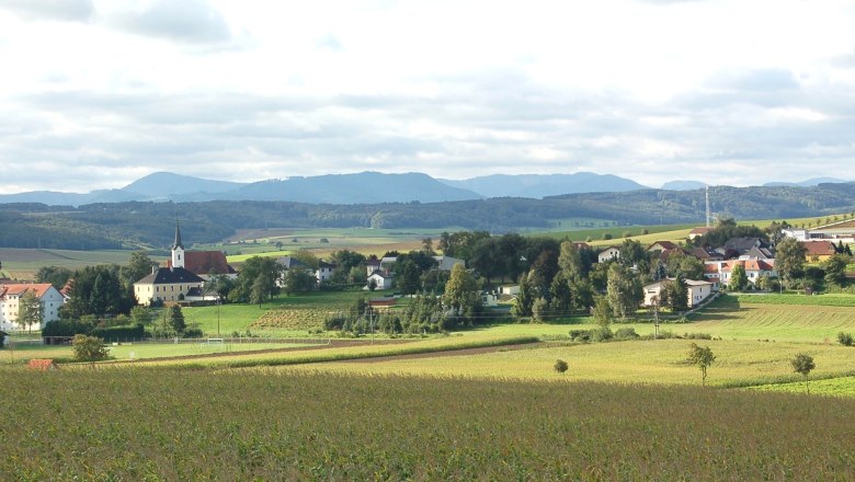 Landscape with village and church in St. Margarethen an der Sierning, surrounded by fields and hills.
