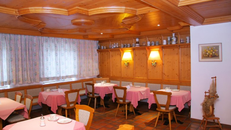 Cozy breakfast room with wooden furniture, pink tablecloths and decorative jugs on a shelf.