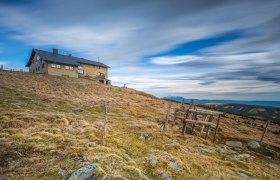 Mountain hut on a hill with a cloudy sky in the background.