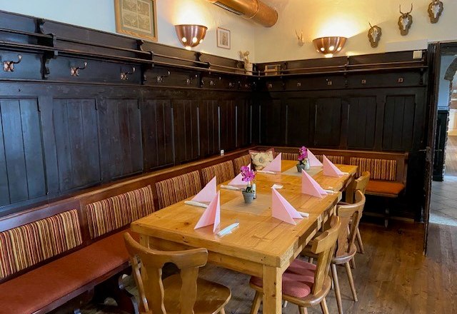 Cozy dining room with wooden table, chairs and bench. Table is decorated with pink napkins and flowers. Dark wood paneling on the walls.