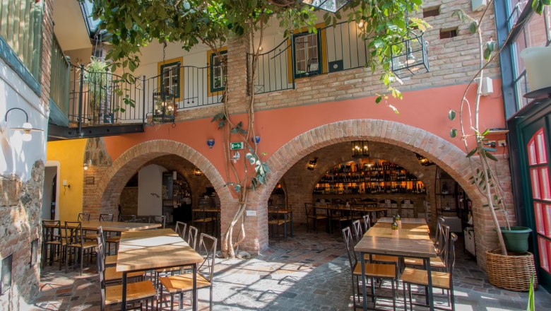 Inner courtyard of a restaurant with tables, chairs and plants, surrounded by brick arches and a balcony.