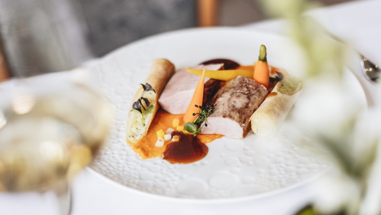 Gourmet dish with pork fillet, vegetables and potato roll on a white plate.