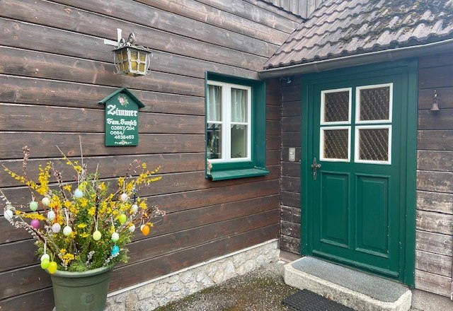 Entrance of a wooden house with green door and window, decorated with an Easter shrub.