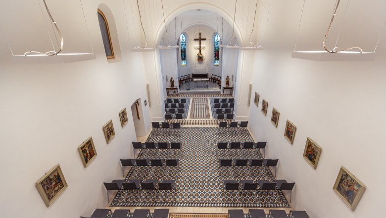 Interior view of a modern chapel with white walls, colorful windows and geometric floor pattern.