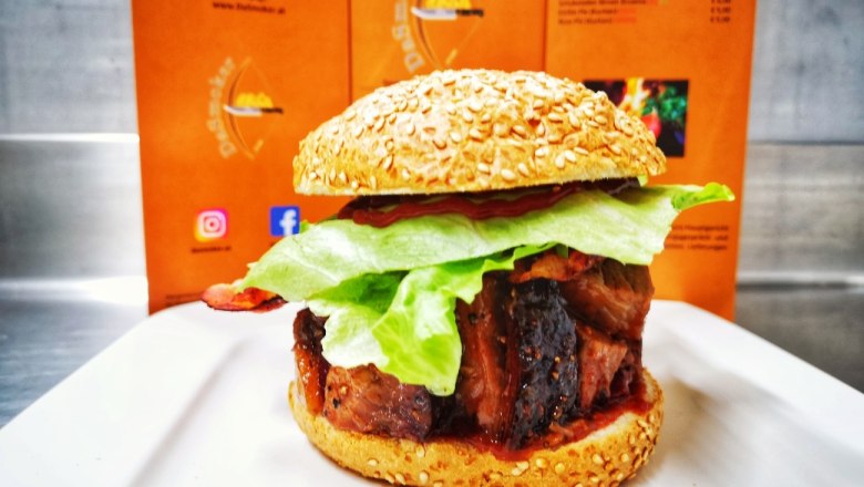 A burger with salad and meat on a white plate in front of an orange-colored menu.