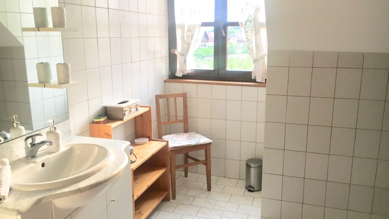Bright bathroom with washbasin, wooden shelf, chair and window with curtains.