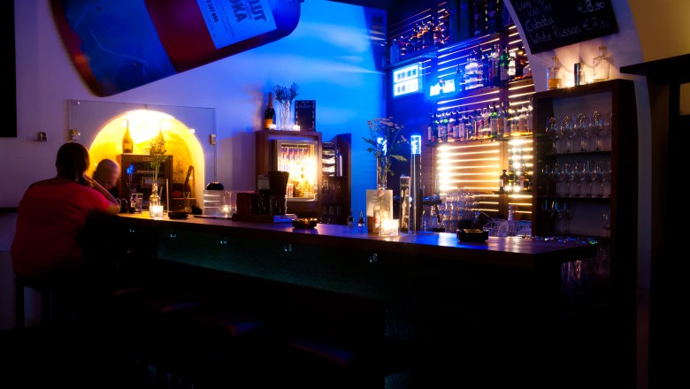 Interior view of a bar with blue lighting and bottle racks.