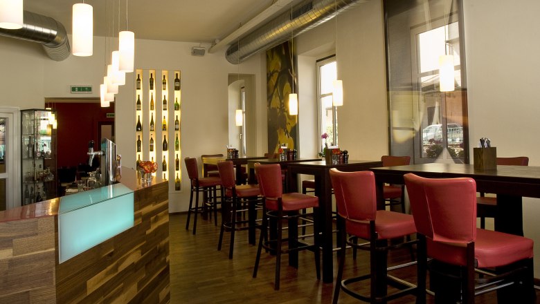 Interior view of a modern restaurant with red chairs and a wooden counter.