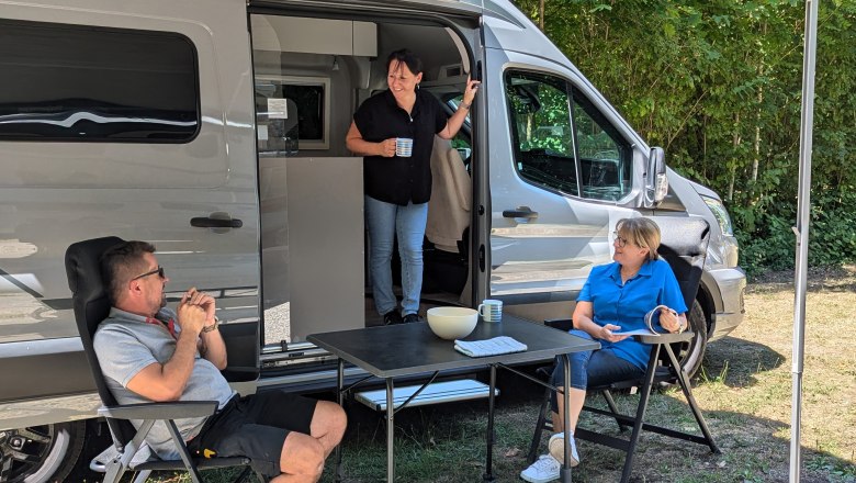 Three people relaxing in front of a mobile home in the open air.