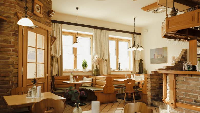 Cozy dining room with wooden furniture and brick walls, decorated with plants and lamps.