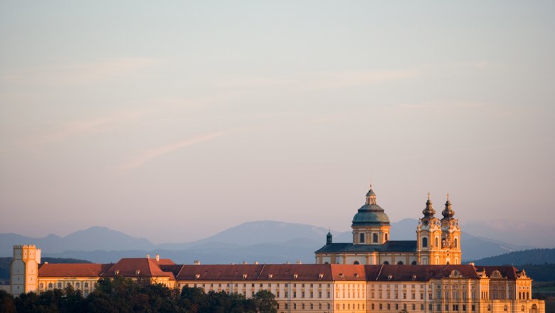 Melk Abbey in Austria at sunset with mountains in the background.