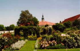 Historic garden with flowers and trees, in the background a building with a tower.