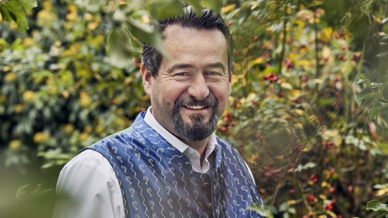 A man in traditional dress smiles in a garden.