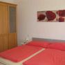 Double bed with red bed linen and brown wardrobe. There is a picture of red flowers above the bed.