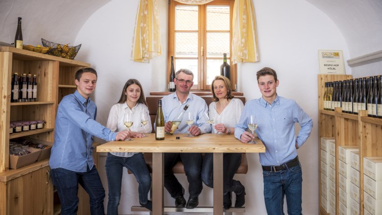 Five people stand around a table in a tasting room with bottles of wine.