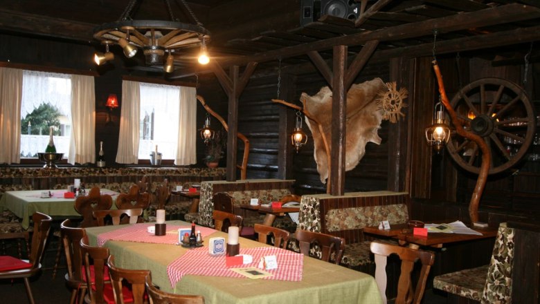 Rustic restaurant with wooden furniture, checkered tablecloths and decorative elements such as wagon wheels and animal fur on the walls.