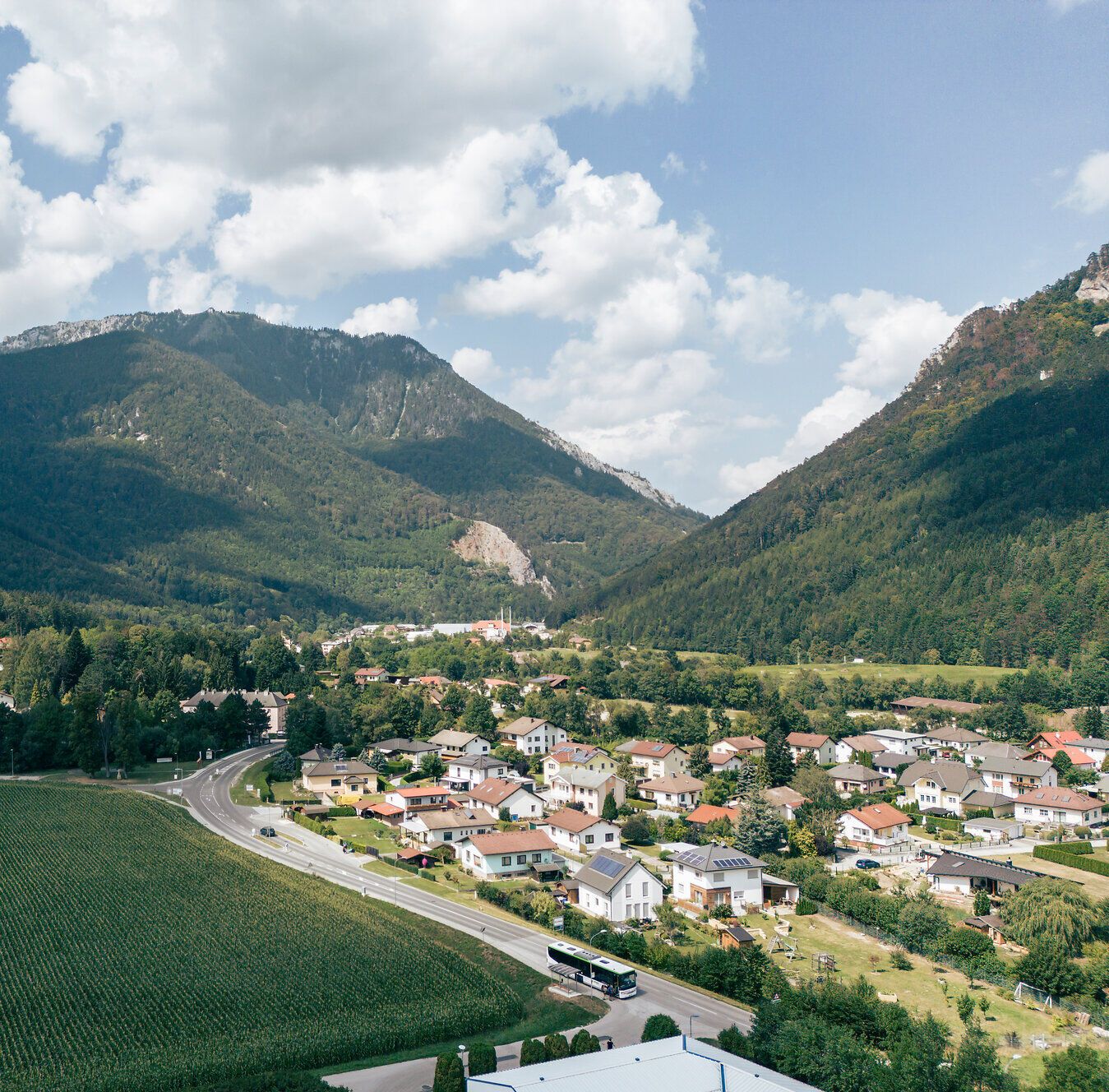 Blick über ein alpines Tal mit Dorf, Feldern und Bergen unter blauem Himmel.