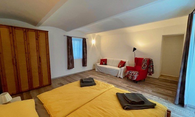 A bedroom with double bed, yellow bed linen, wooden wardrobe, red armchair and white sofa.