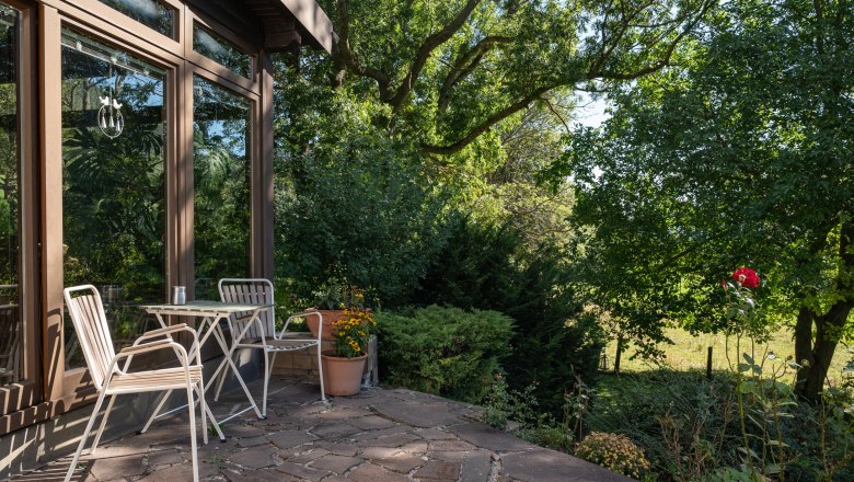 Terrace with table and chairs in front of a vacation home, surrounded by trees and plants.