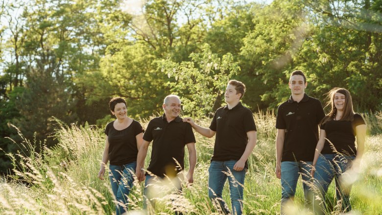 A smiling family strolls through a green meadow in the sunshine.