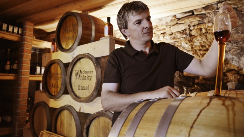 A man tasting whisky in a storage room with barrels.