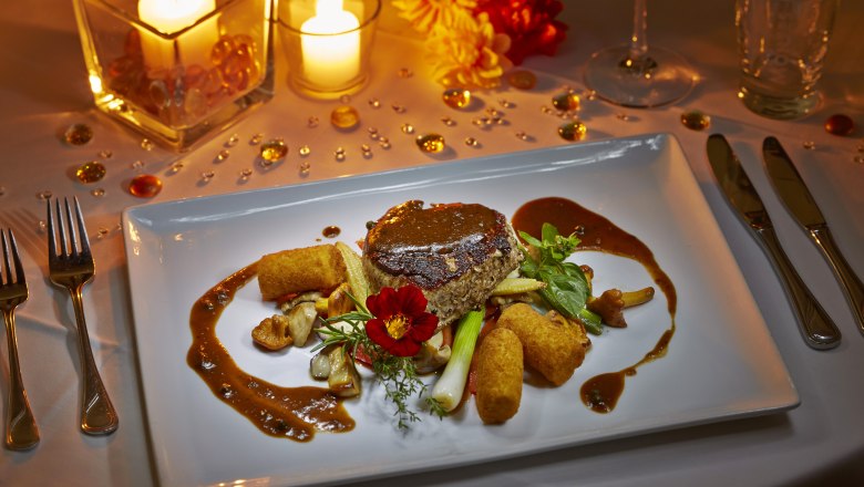 An elegant dish on a white plate, surrounded by candlelight and decorative elements.