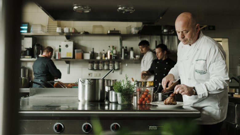 Cooks work in a professional kitchen, one cuts meat.