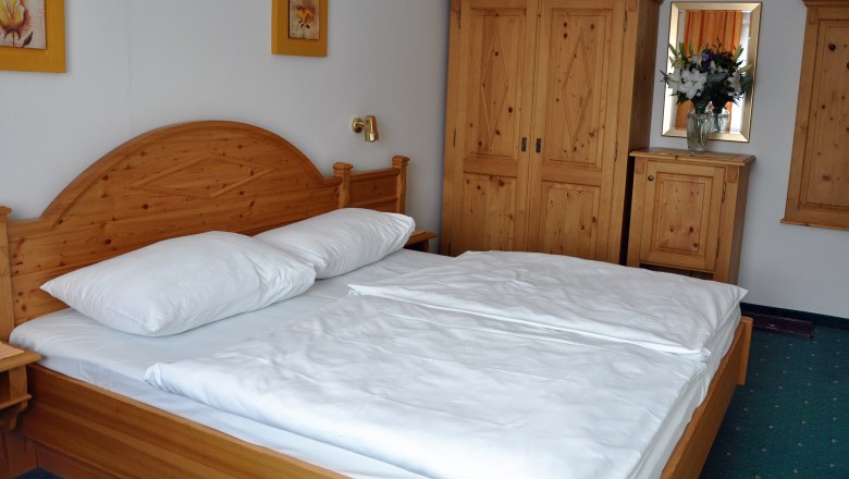 Comfort room with solid wood furniture, double bed, closet and flowers on chest of drawers.