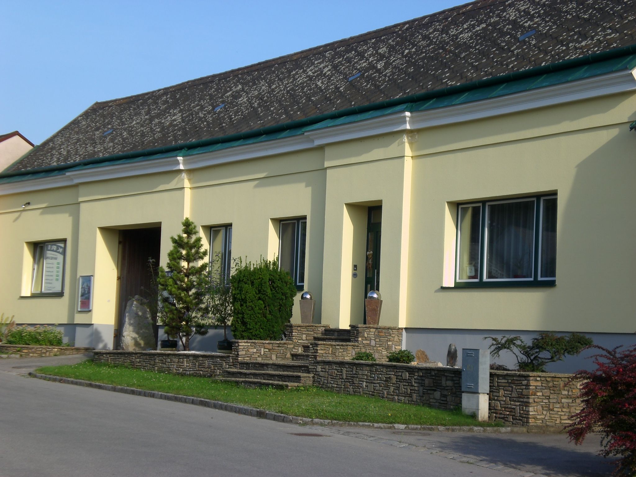 Yellow building with stone wall and plants in front of the entrance.