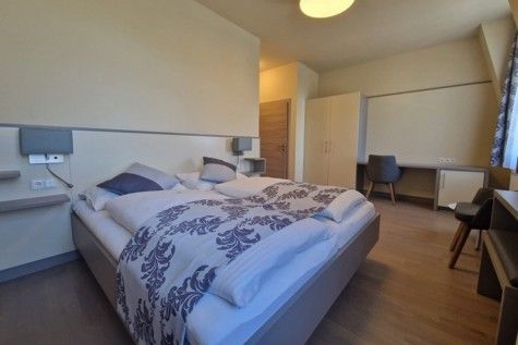 Modern furnished hotel room with double bed, desk and closet.