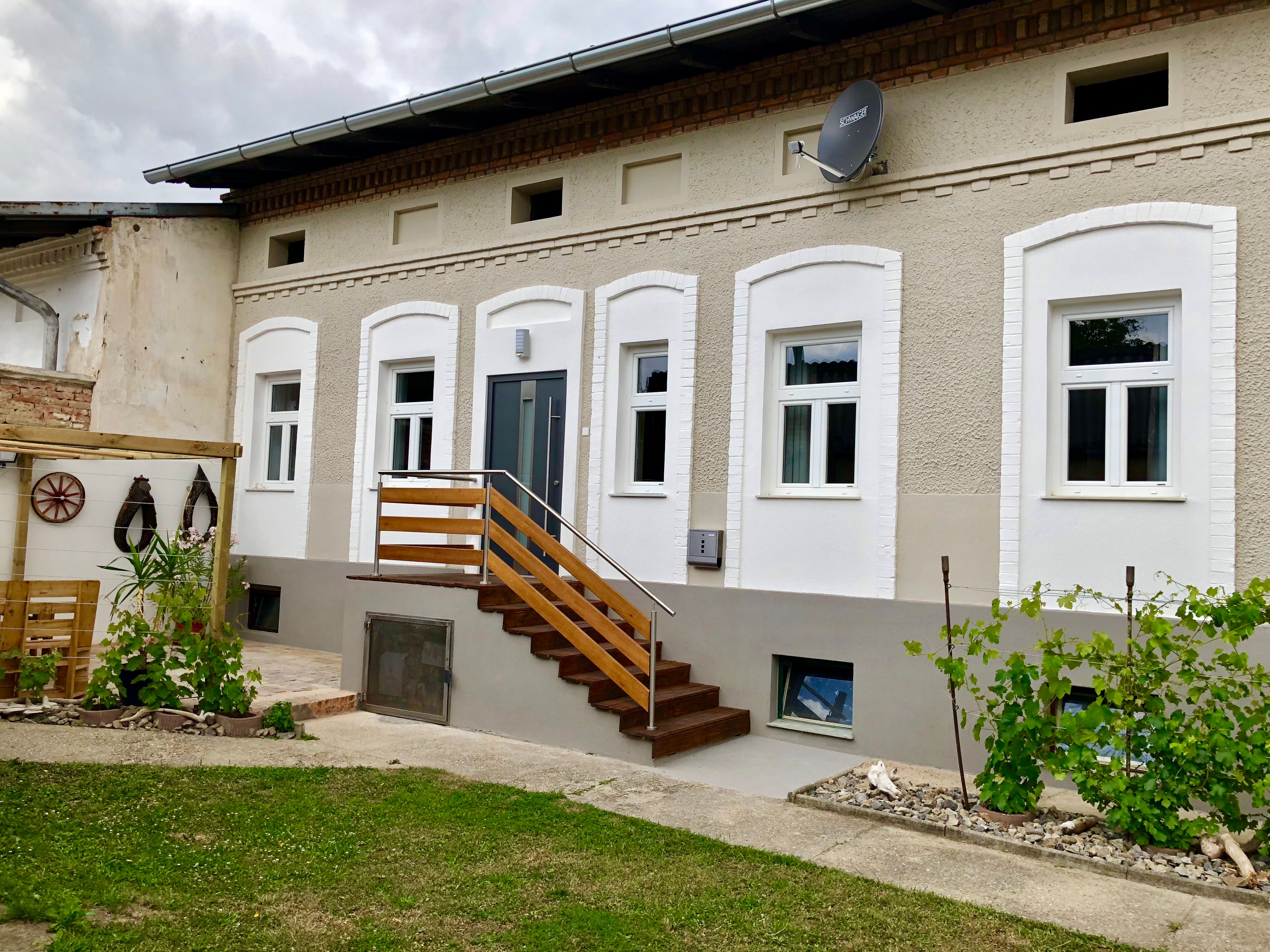 A renovated house with white windows and a wooden staircase, surrounded by a small garden with plants.