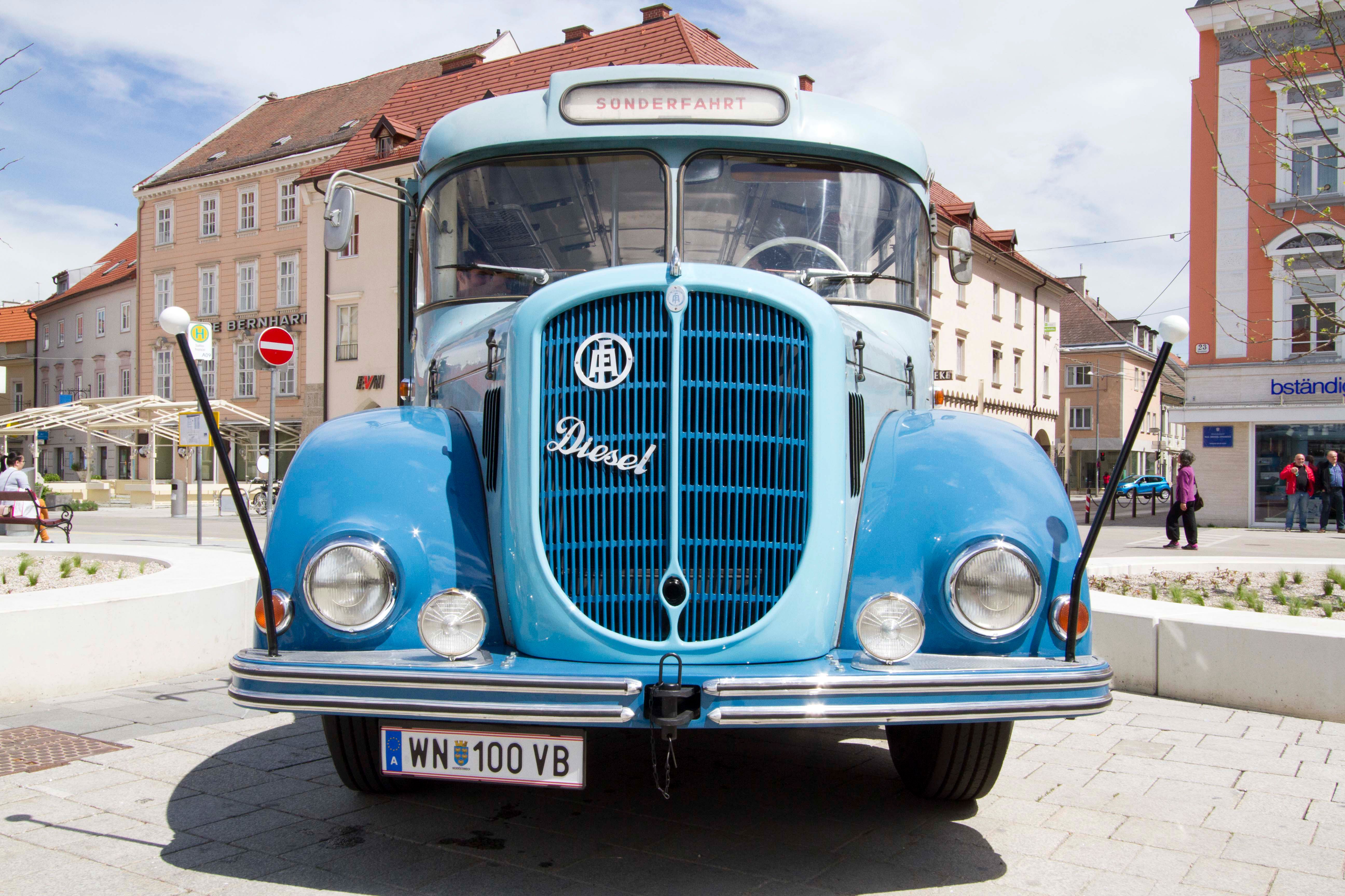 A blue vintage bus from 1961 is parked on a square in front of buildings.