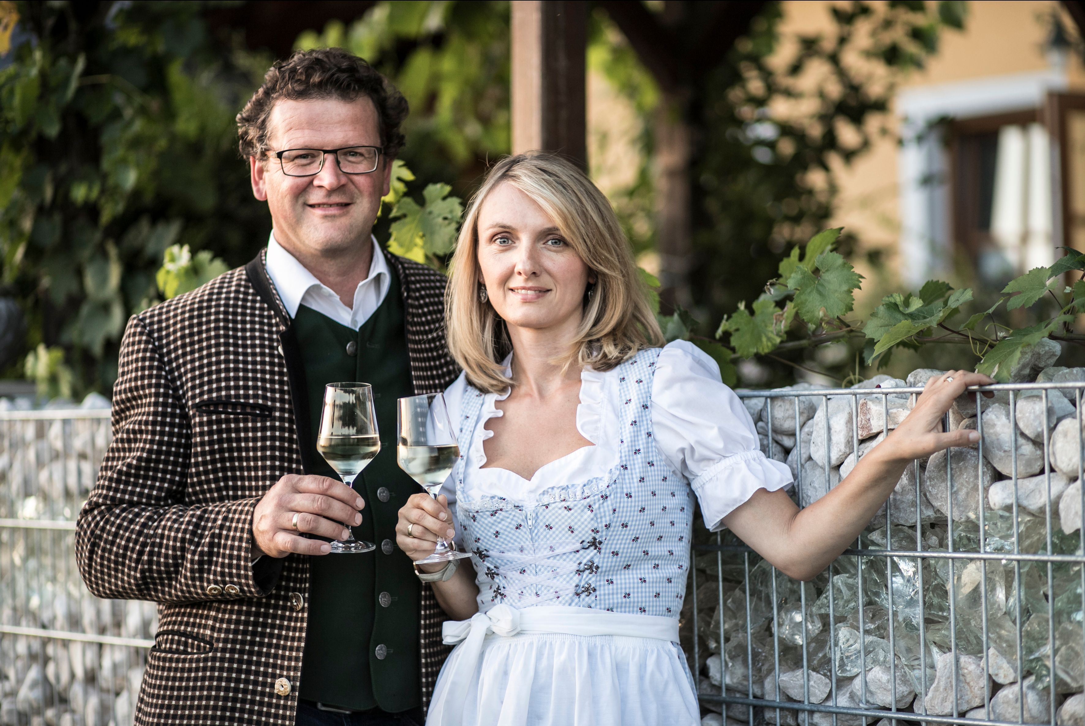 A man and a woman in traditional dress are holding wine glasses.