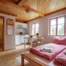 Cozy vacation apartment with wooden floor, double bed, small kitchen and dining table. Bathroom in the background.