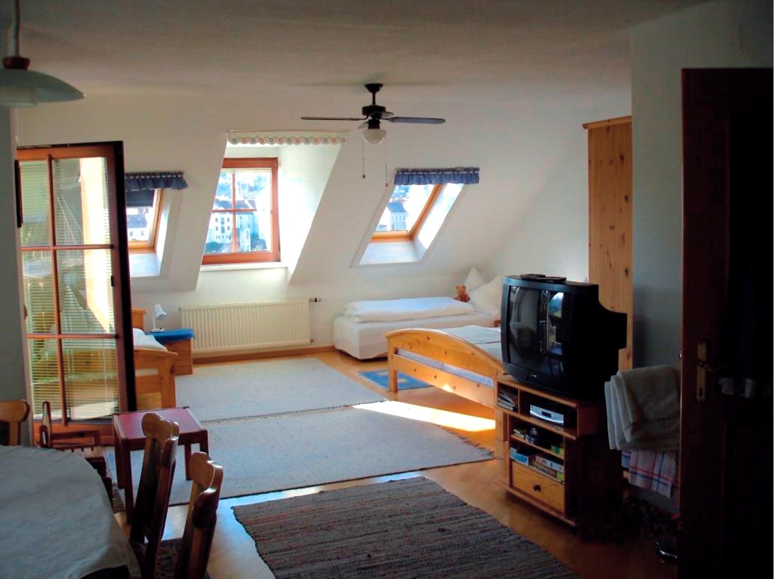 Interior view of a cozy attic room with wooden furniture, two beds, a TV and skylights.