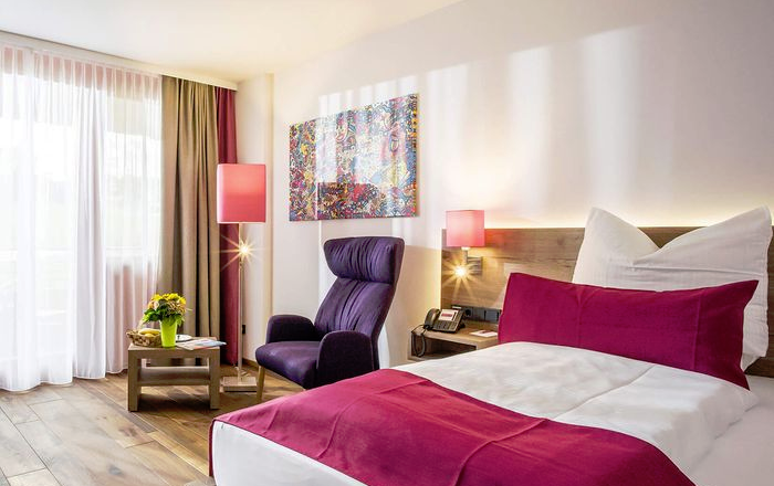 Cozy room with double bed, wing chair, table, lamps, a mural and wooden floor.