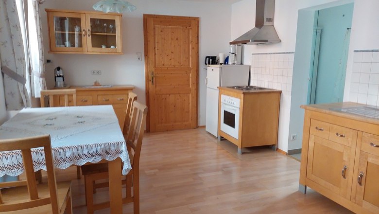 Kitchen with wooden furniture, dining table, chairs, stove, fridge and wall cupboard.