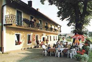 An inn with a terrace where people sit at tables surrounded by parasols and flowers.