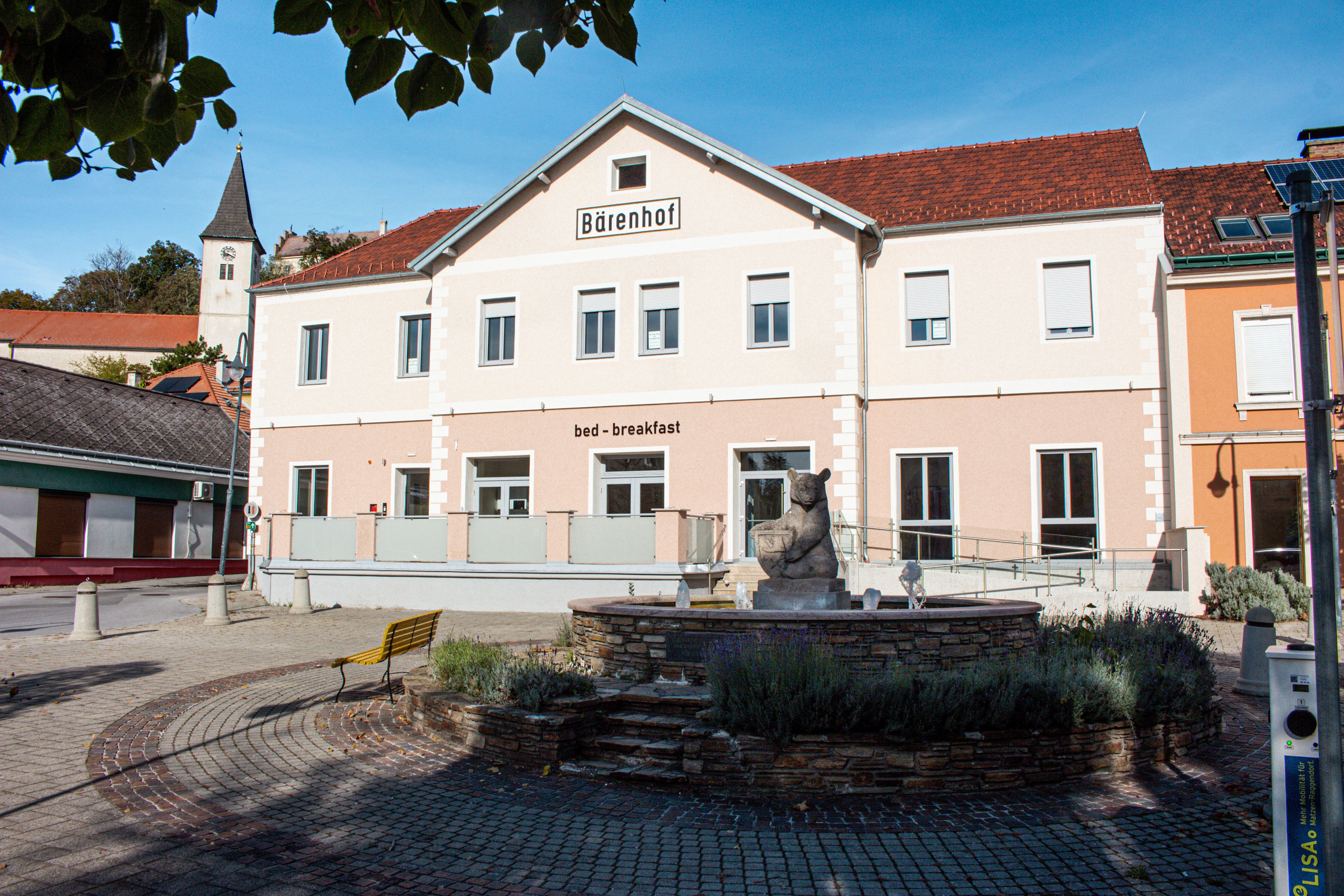 A building with the inscription 'Bärenhof' and 'bed - breakfast' in a sunny setting with a fountain in the foreground.