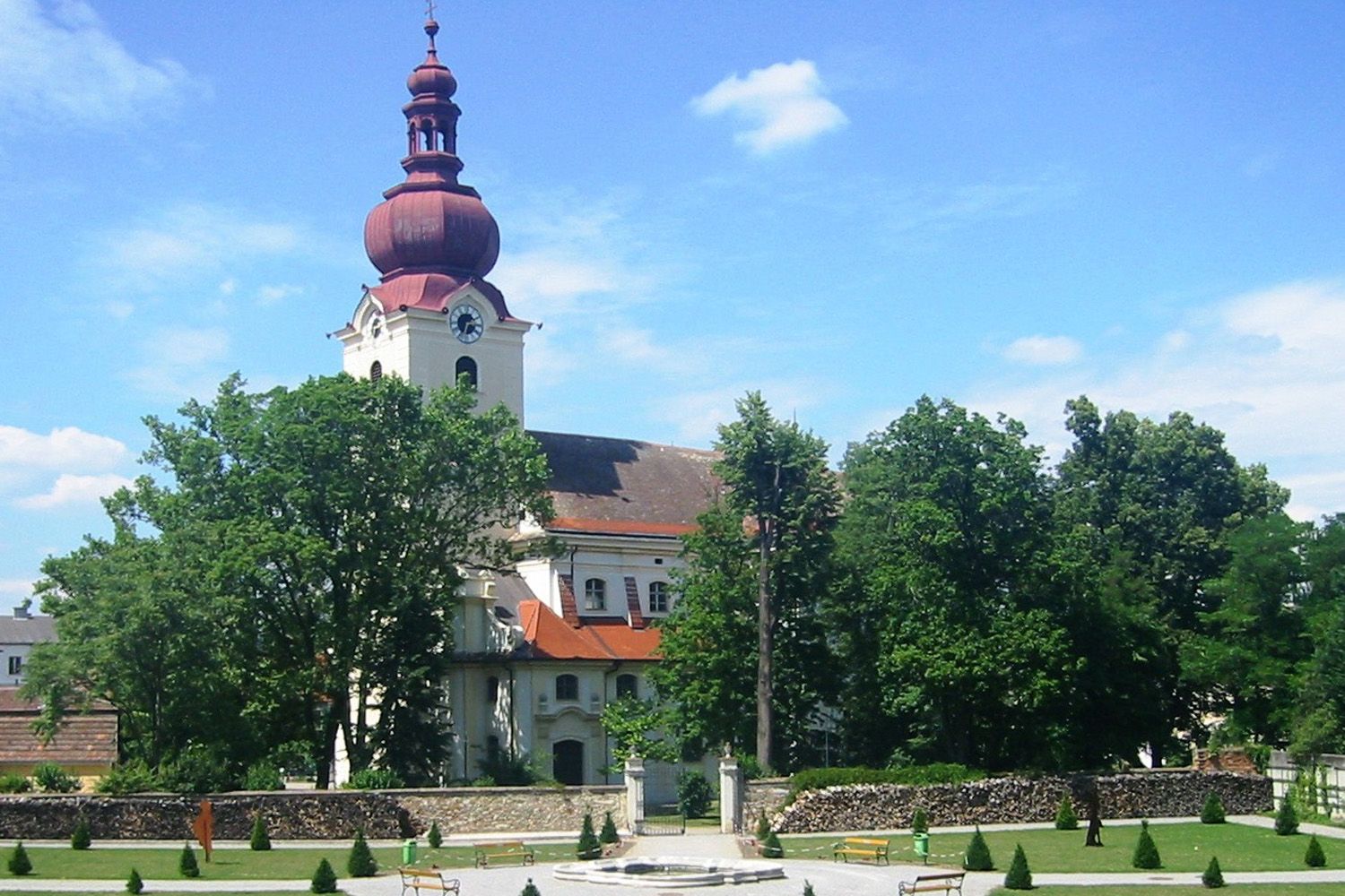 Baroque church with red tower and baroque garden in the foreground.