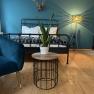 Bedroom with blue armchair, metal bed, plant on table and floor lamp.