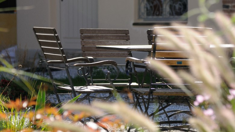 An inner courtyard with a table and chairs made of wood and metal, surrounded by plants and a building in the background.