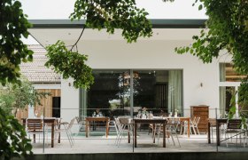 Terrace with tables and chairs, surrounded by green trees.