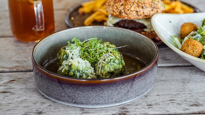 A plate with spinach dumplings, parmesan and cress. In the background, a drink, a burger and a salad.