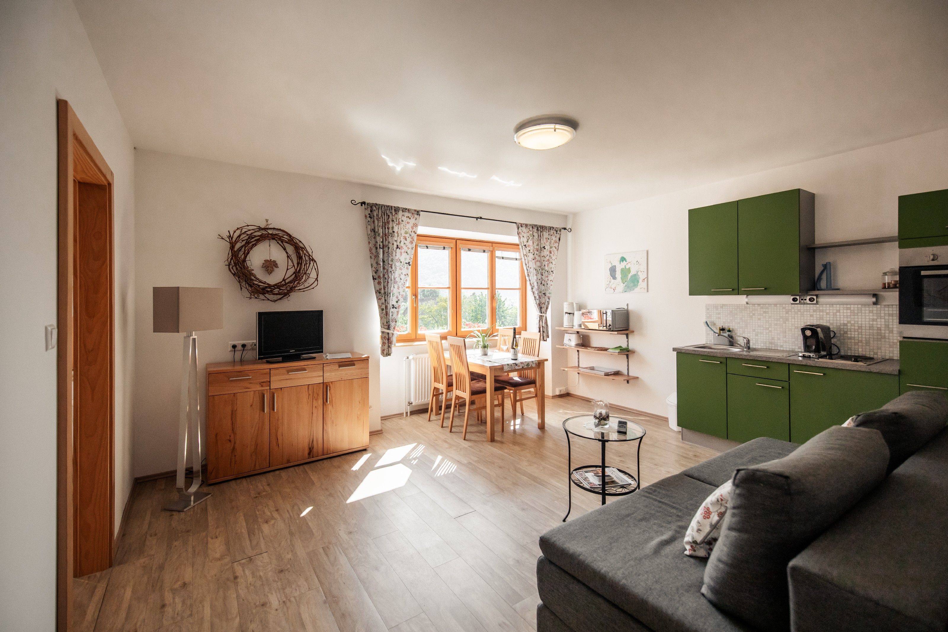Bright living room with green kitchen, dining table and sofa.